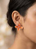 Close-up of a person wearing an orange flower-shaped earring with a blurred background
