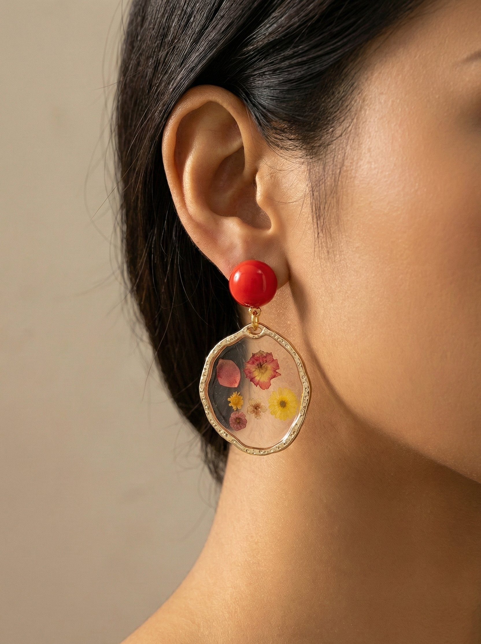 Close-up of a person wearing a floral earring with a red gemstone on a beige background