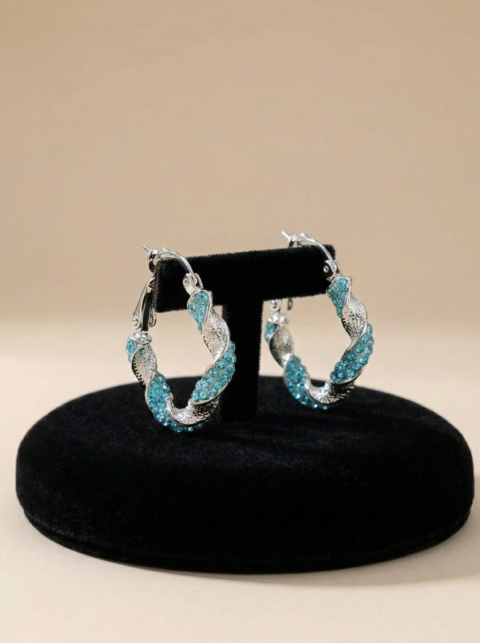Pair of hoop earrings with turquoise stones on a black stand against a beige background
