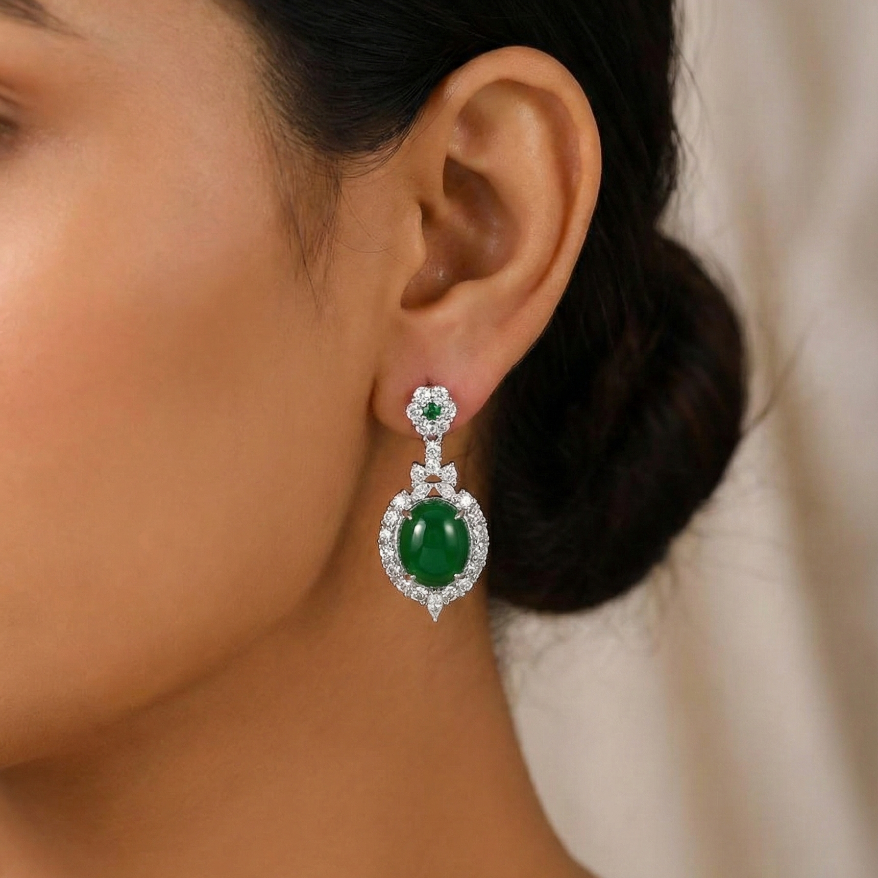 Close-up of a person wearing emerald green earrings with a neutral background