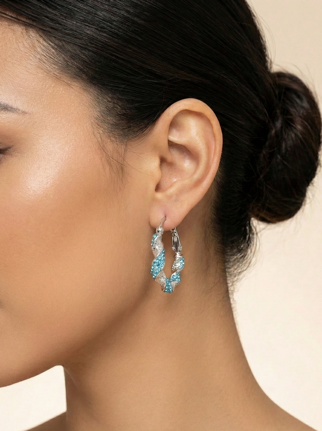 Close-up of a woman wearing a pair of hoop earrings with blue gemstones on a neutral background.