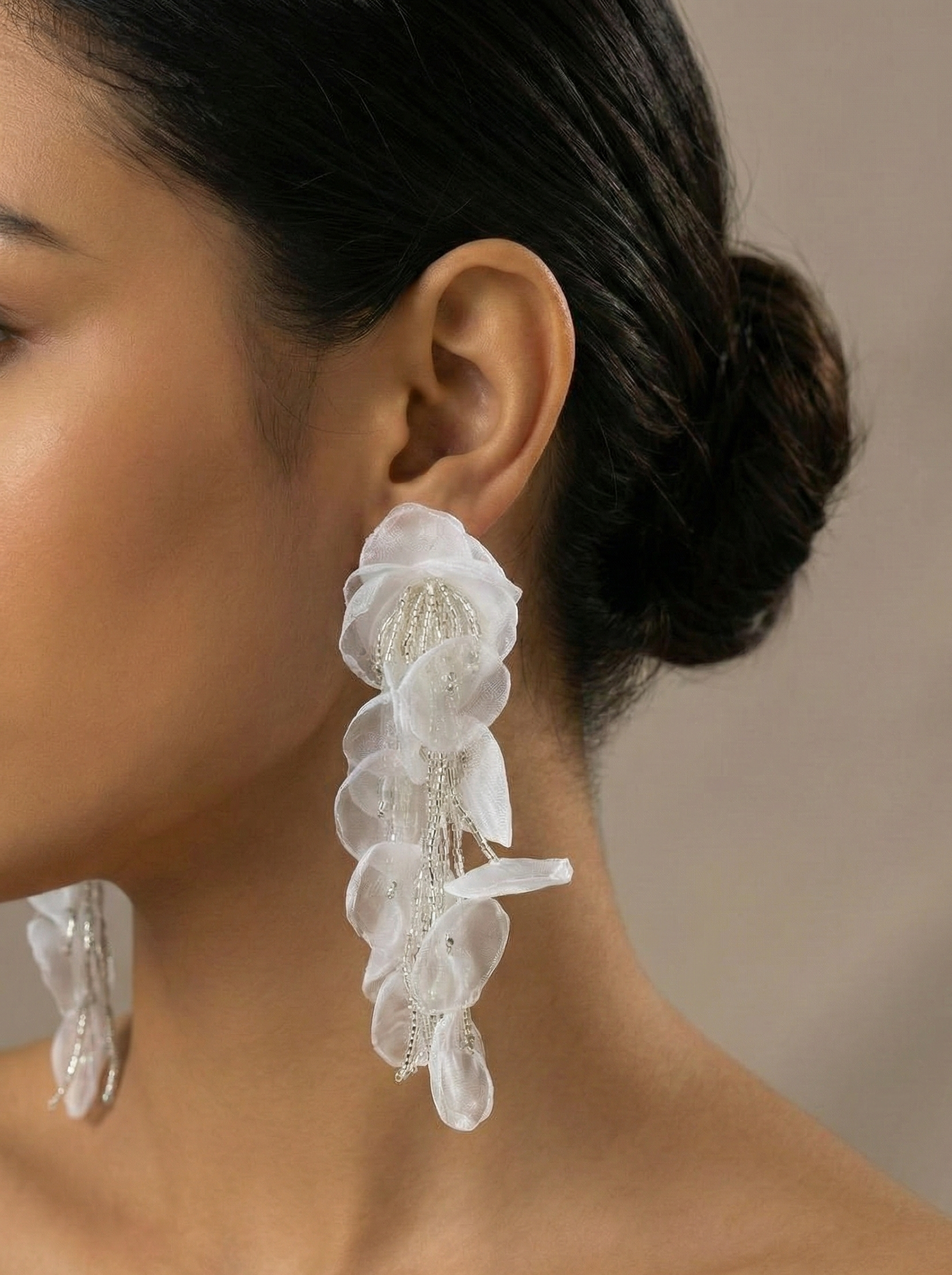 Close-up of a woman wearing elegant white floral earrings against a neutral background