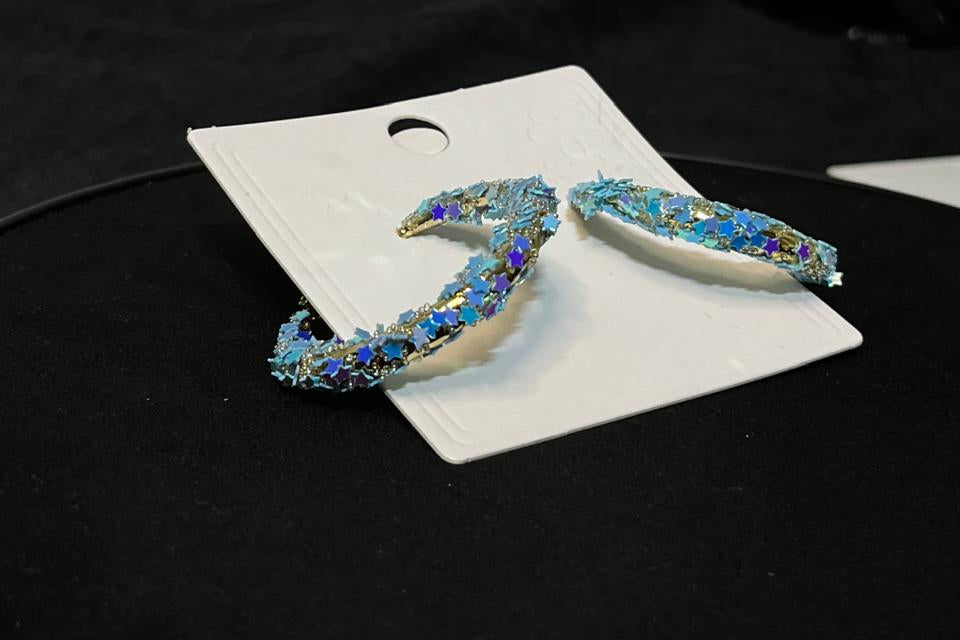 Decorative earrings with blue gemstones on a white card, placed on a black surface.